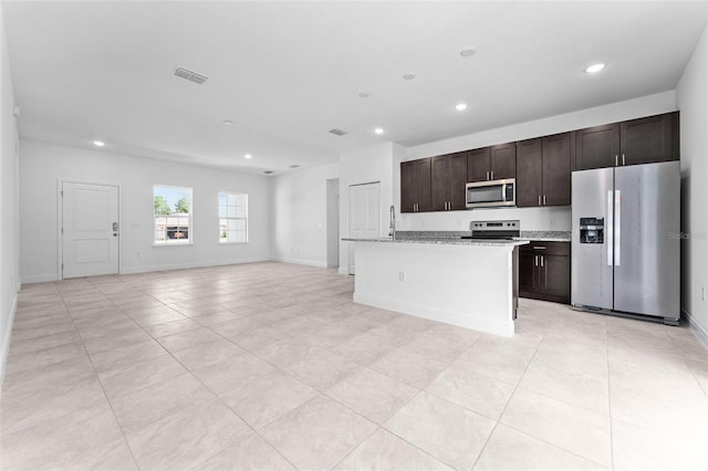 kitchen with dark brown cabinetry, appliances with stainless steel finishes, light tile flooring, and a kitchen island with sink