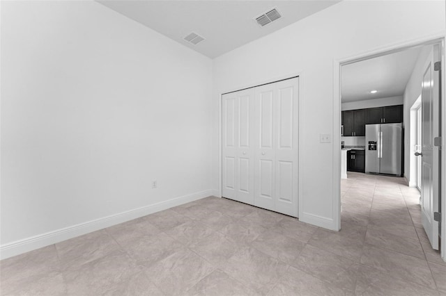 unfurnished bedroom with stainless steel fridge with ice dispenser, a closet, and light tile floors