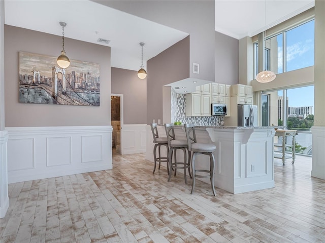 kitchen with a breakfast bar, hanging light fixtures, appliances with stainless steel finishes, light hardwood / wood-style floors, and light stone counters