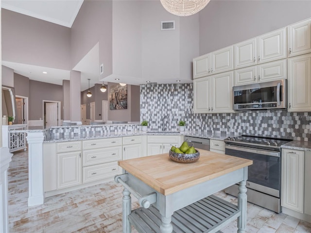 kitchen featuring kitchen peninsula, appliances with stainless steel finishes, a towering ceiling, tasteful backsplash, and light stone counters