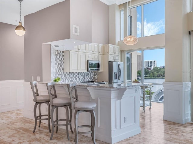 kitchen with light stone countertops, appliances with stainless steel finishes, kitchen peninsula, hanging light fixtures, and a breakfast bar area