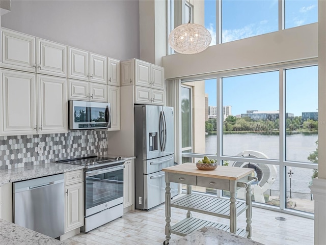 kitchen featuring decorative backsplash, light stone countertops, stainless steel appliances, a water view, and white cabinetry