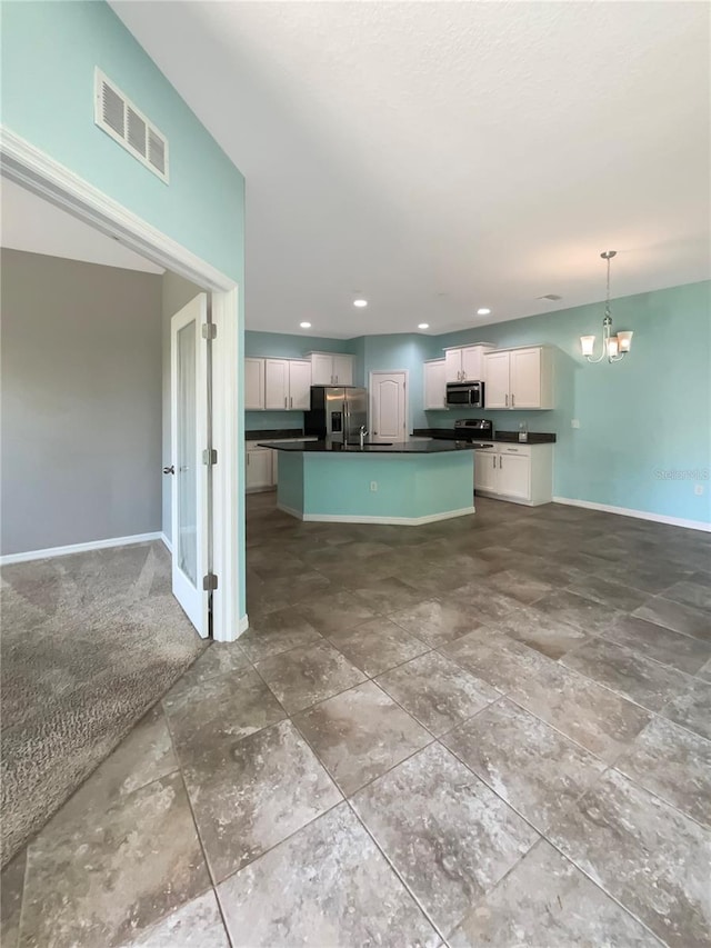 kitchen featuring appliances with stainless steel finishes, white cabinetry, a chandelier, a center island with sink, and pendant lighting