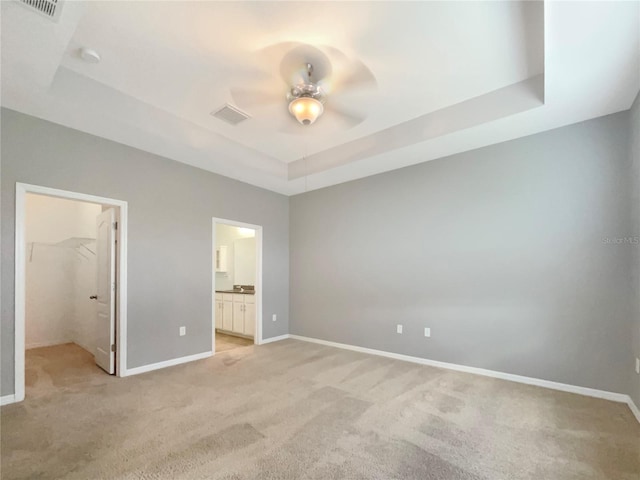 unfurnished bedroom featuring a closet, a spacious closet, a raised ceiling, and light colored carpet