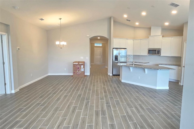 kitchen with stone counters, a kitchen island with sink, white cabinetry, stainless steel appliances, and light wood-type flooring