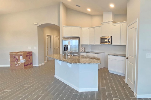 kitchen featuring sink, white cabinetry, a center island with sink, dark stone counters, and stainless steel appliances