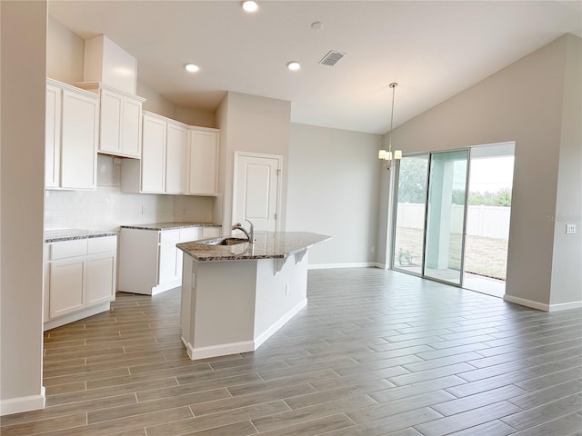 kitchen featuring sink, stone counters, a kitchen island with sink, tasteful backsplash, and white cabinets