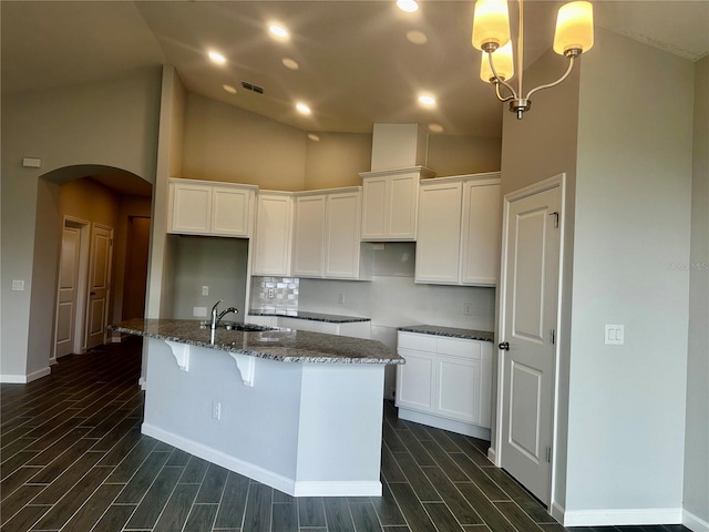 kitchen featuring dark stone countertops, sink, an island with sink, and white cabinets