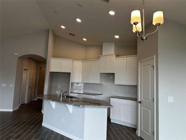 kitchen featuring white cabinetry, a kitchen island with sink, sink, and dark stone counters