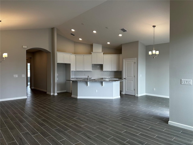 kitchen with dark wood-type flooring, white cabinetry, an island with sink, decorative backsplash, and a chandelier