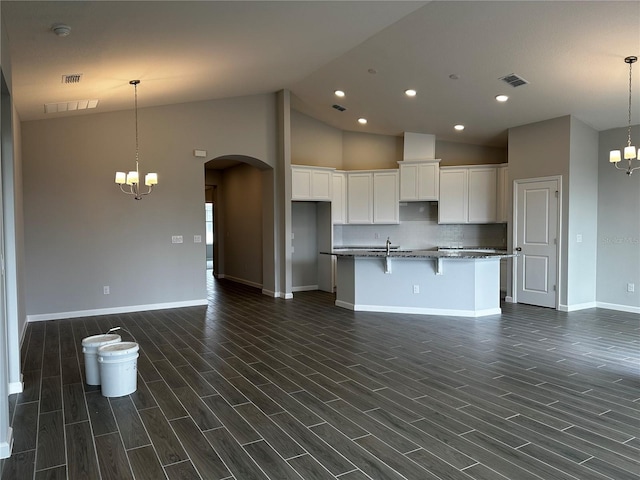 kitchen featuring a notable chandelier, a kitchen island with sink, white cabinets, and dark stone counters