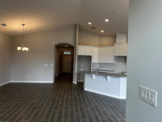 kitchen with a kitchen bar, dark hardwood / wood-style floors, white cabinets, dark stone counters, and backsplash