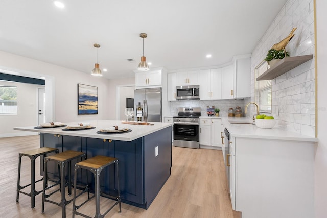 kitchen with sink, a kitchen island, pendant lighting, white cabinets, and appliances with stainless steel finishes