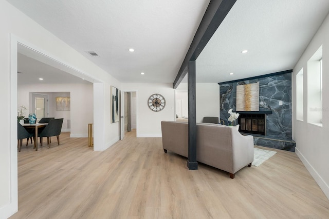 living room with a stone fireplace, light hardwood / wood-style floors, and a textured ceiling