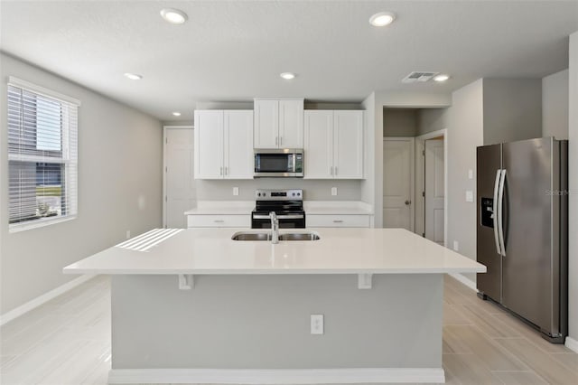 kitchen featuring appliances with stainless steel finishes, a kitchen breakfast bar, a kitchen island with sink, sink, and white cabinetry