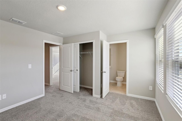 unfurnished bedroom with a textured ceiling, ensuite bathroom, light carpet, and a closet