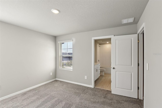 unfurnished bedroom with a textured ceiling, ensuite bathroom, and light colored carpet