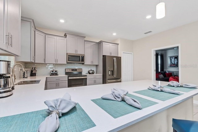 kitchen with sink, kitchen peninsula, pendant lighting, decorative backsplash, and appliances with stainless steel finishes