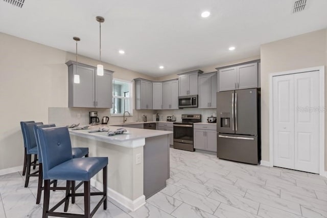 kitchen with a kitchen bar, kitchen peninsula, stainless steel appliances, pendant lighting, and gray cabinets