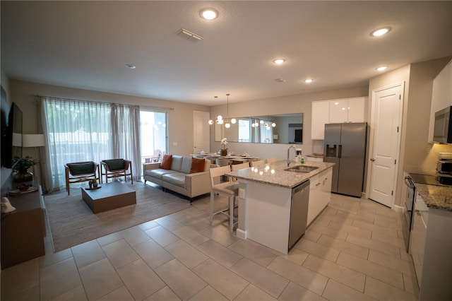 kitchen with stainless steel appliances, sink, decorative light fixtures, white cabinets, and an island with sink