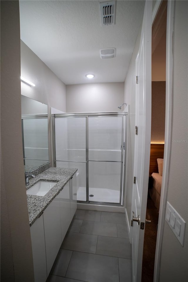 bathroom with tile patterned floors, vanity, a shower with shower door, and a textured ceiling