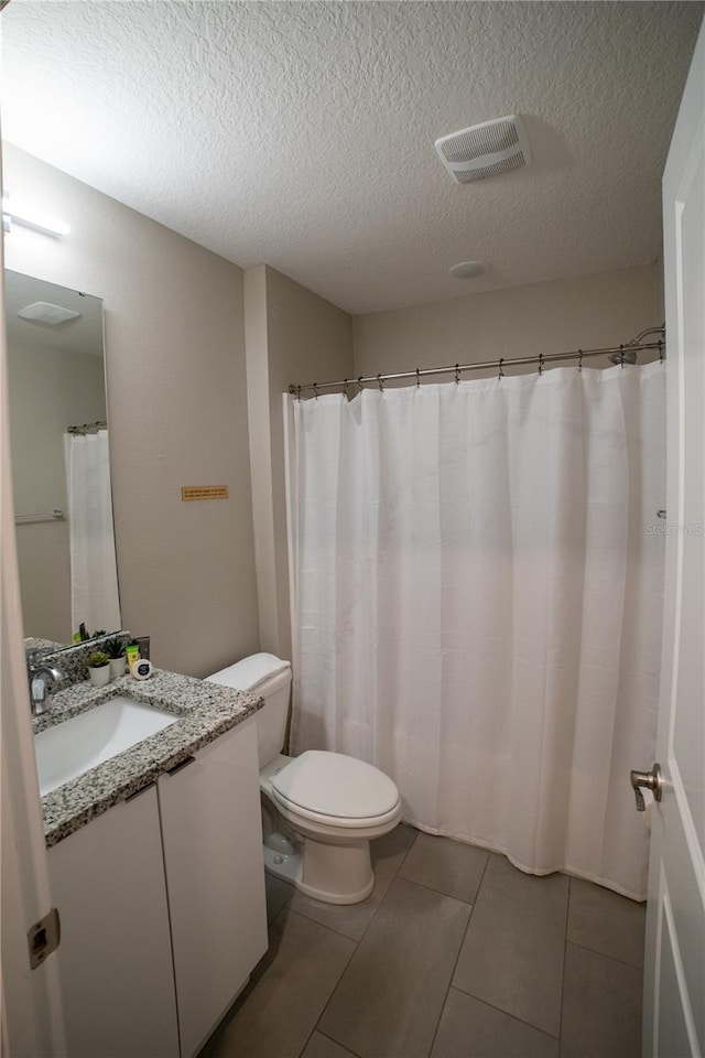 bathroom featuring tile patterned flooring, vanity, toilet, and a textured ceiling