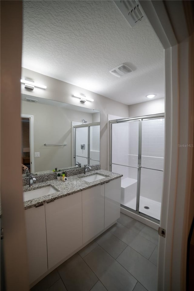 bathroom with tile patterned floors, vanity, an enclosed shower, and a textured ceiling