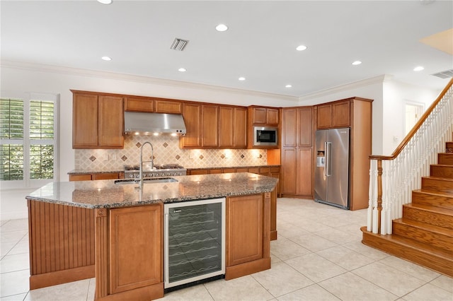 kitchen featuring light tile floors, wine cooler, backsplash, stainless steel appliances, and a kitchen island with sink