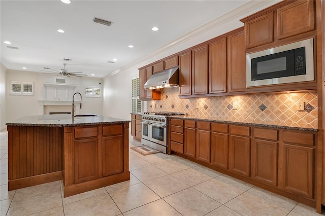 kitchen with range with two ovens, backsplash, wall chimney range hood, a center island with sink, and black microwave