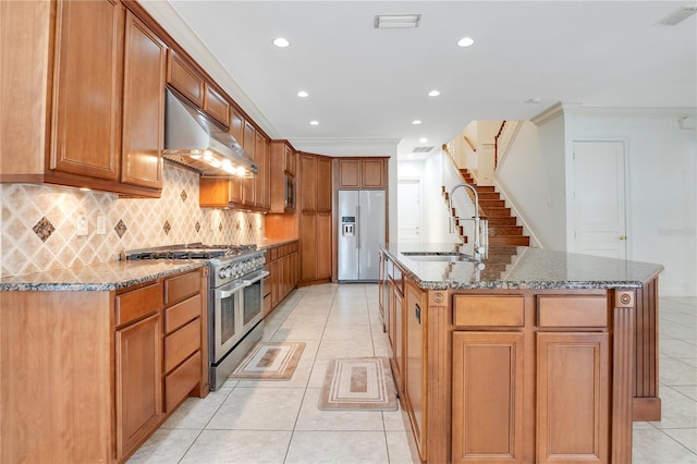 kitchen featuring appliances with stainless steel finishes, an island with sink, wall chimney exhaust hood, sink, and light tile floors