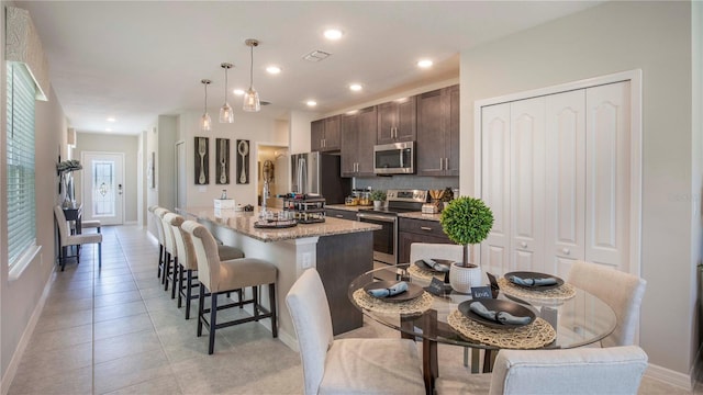 kitchen featuring appliances with stainless steel finishes, a breakfast bar, pendant lighting, dark brown cabinetry, and a center island with sink