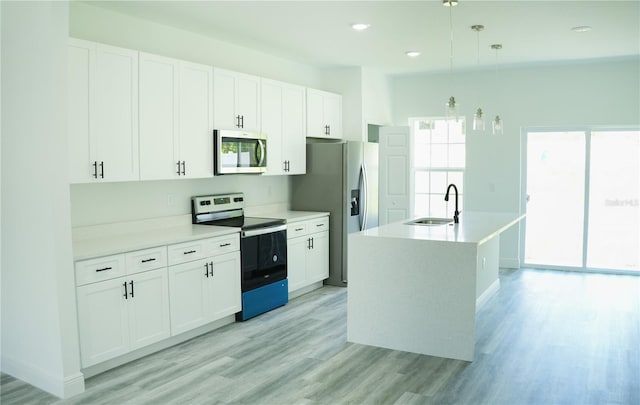 kitchen featuring light wood-type flooring, white cabinetry, stainless steel appliances, sink, and an island with sink