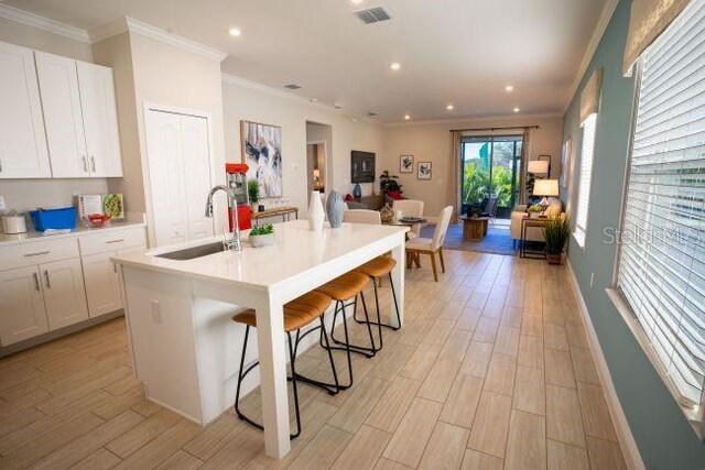 kitchen featuring sink, a breakfast bar, a kitchen island with sink, light hardwood / wood-style floors, and white cabinets