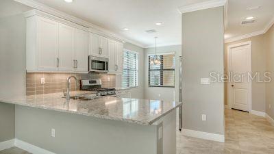 kitchen with kitchen peninsula, appliances with stainless steel finishes, tasteful backsplash, light stone counters, and white cabinets