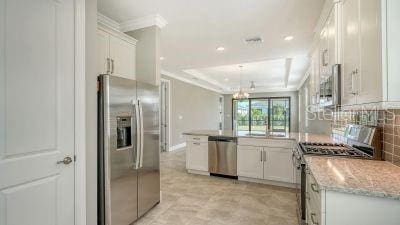 kitchen featuring light stone countertops, white cabinetry, stainless steel appliances, backsplash, and a tray ceiling