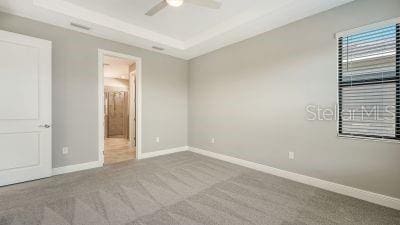 unfurnished bedroom featuring light colored carpet, a raised ceiling, and ceiling fan