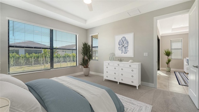 carpeted bedroom featuring multiple windows, a tray ceiling, and ceiling fan