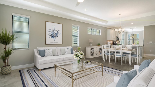 living room with ceiling fan with notable chandelier and a tray ceiling