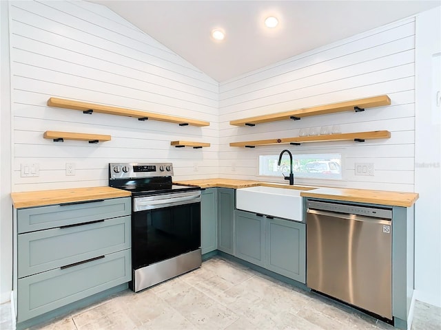 kitchen with appliances with stainless steel finishes, light tile floors, wooden counters, sink, and vaulted ceiling