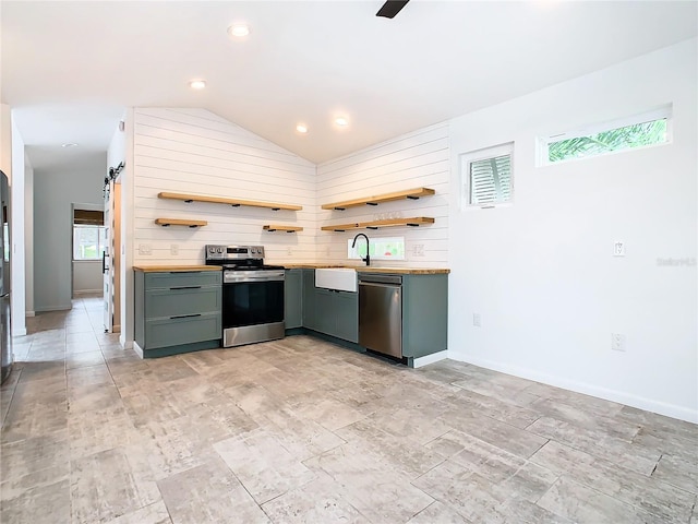 kitchen with stainless steel appliances, light tile flooring, sink, wood walls, and lofted ceiling