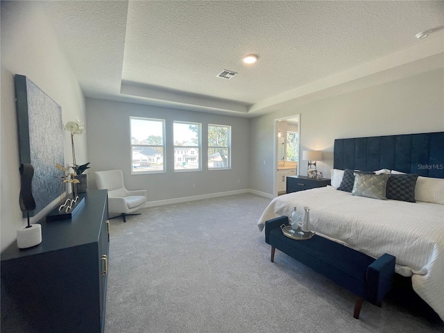 bedroom featuring connected bathroom, light carpet, a textured ceiling, and a tray ceiling