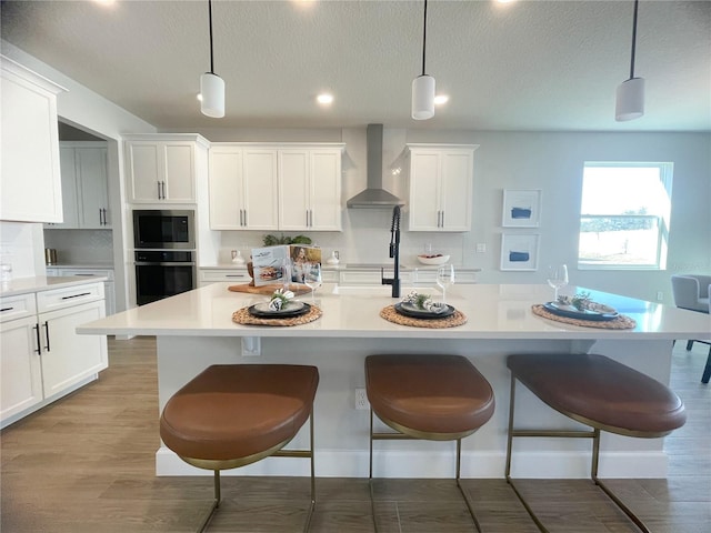 kitchen featuring pendant lighting, wall chimney range hood, and wall oven