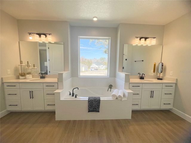 bathroom featuring vanity, wood-type flooring, tiled bath, and a textured ceiling