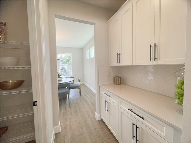 bar with backsplash, light hardwood / wood-style floors, and white cabinets