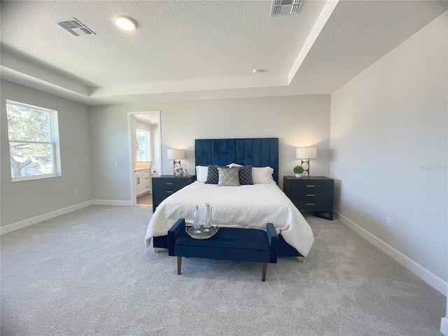 carpeted bedroom featuring a raised ceiling, ensuite bathroom, and a textured ceiling