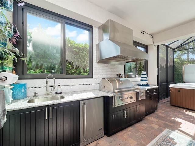 kitchen with tasteful backsplash, fridge, wall chimney exhaust hood, a healthy amount of sunlight, and sink