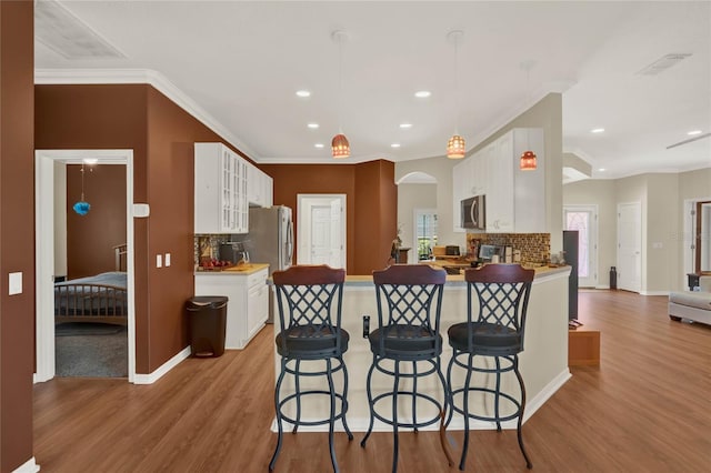 kitchen with backsplash, a kitchen bar, light wood-type flooring, white cabinets, and pendant lighting