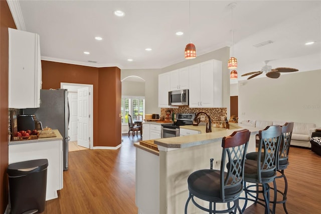 kitchen featuring hanging light fixtures, light hardwood / wood-style flooring, kitchen peninsula, and appliances with stainless steel finishes