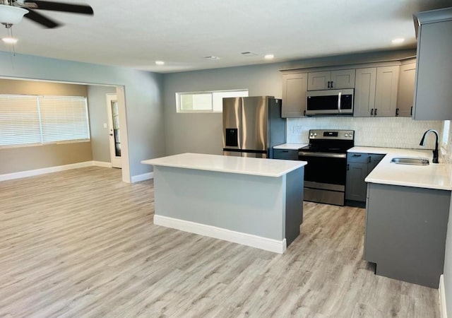 kitchen with appliances with stainless steel finishes, a kitchen island, sink, light hardwood / wood-style floors, and tasteful backsplash