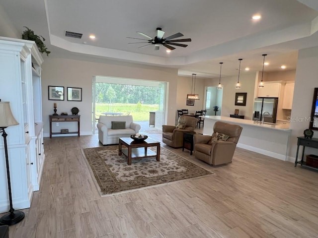 living room with ceiling fan, a raised ceiling, and light hardwood / wood-style flooring